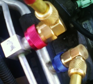 Shown at the ends of low- and high-pressure lines in this photo are “automatic” coupling pieces after being connected to a vehicle’s a/c system. Blue or red colored lock rings on the couplers lock in place automatically during fastening, then release when slid upward by hand.