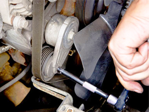 Visible in this photo is a spring-loaded serpentine belt tensioner. This type of tensioner never needs adjustment and will release its tension when force is placed against it using proper hand tools if the belt needs to be removed or replaced