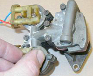 (Caption for above photo: In this picture, a throttle body has been removed from the engine with electrical connectors in place. To remove the injectors, unbolt any hold-down screws or nuts. Grab the center of the injectors with a pair of pliers and rotate in order to break them loose and remove.