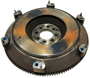 This flywheel from a 2010 Dodge Challenger has developed severe warpage. The dark spots visible here are the high spots on the flywheel which became ground down due to excessive slippage. The clutch and throwout bearing of this car became completely destroyed as a result.